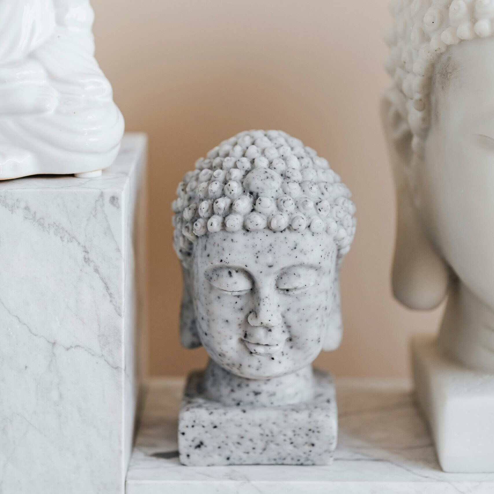 Small bust of Buddha with closed eyes and bubbly headdress made of speckled marble near Asian sculpture collection on beige background