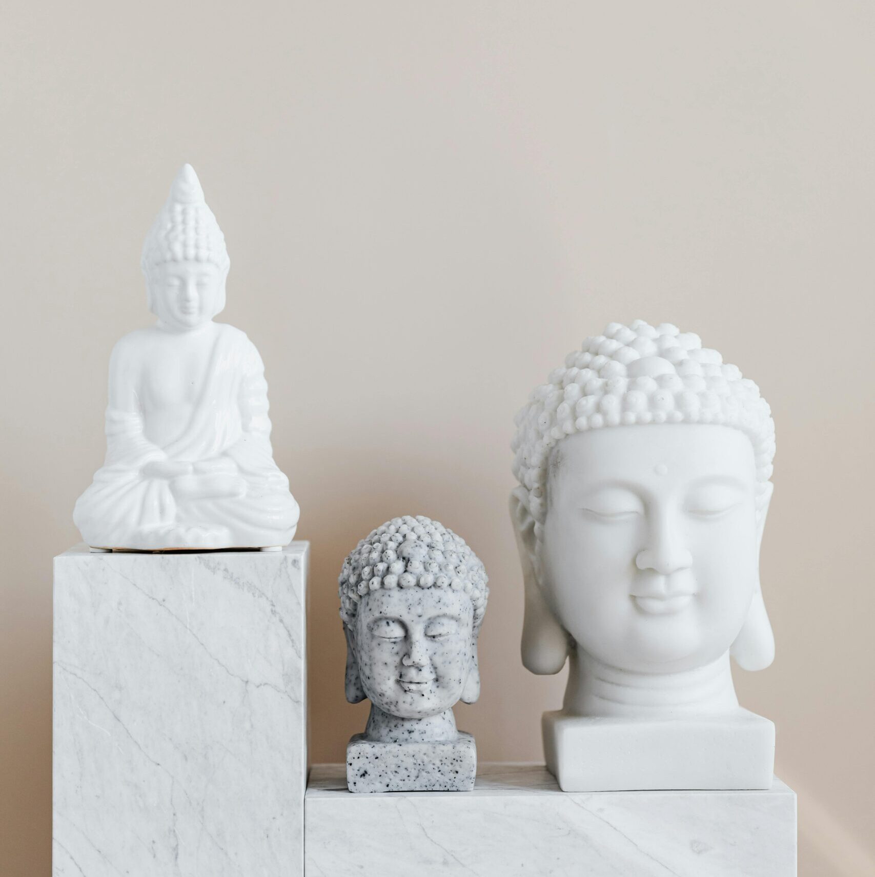 Set of various gypsum and stone Buddha sculptures placed on white marble shelf against beige wall as home decoration element and religion symbol