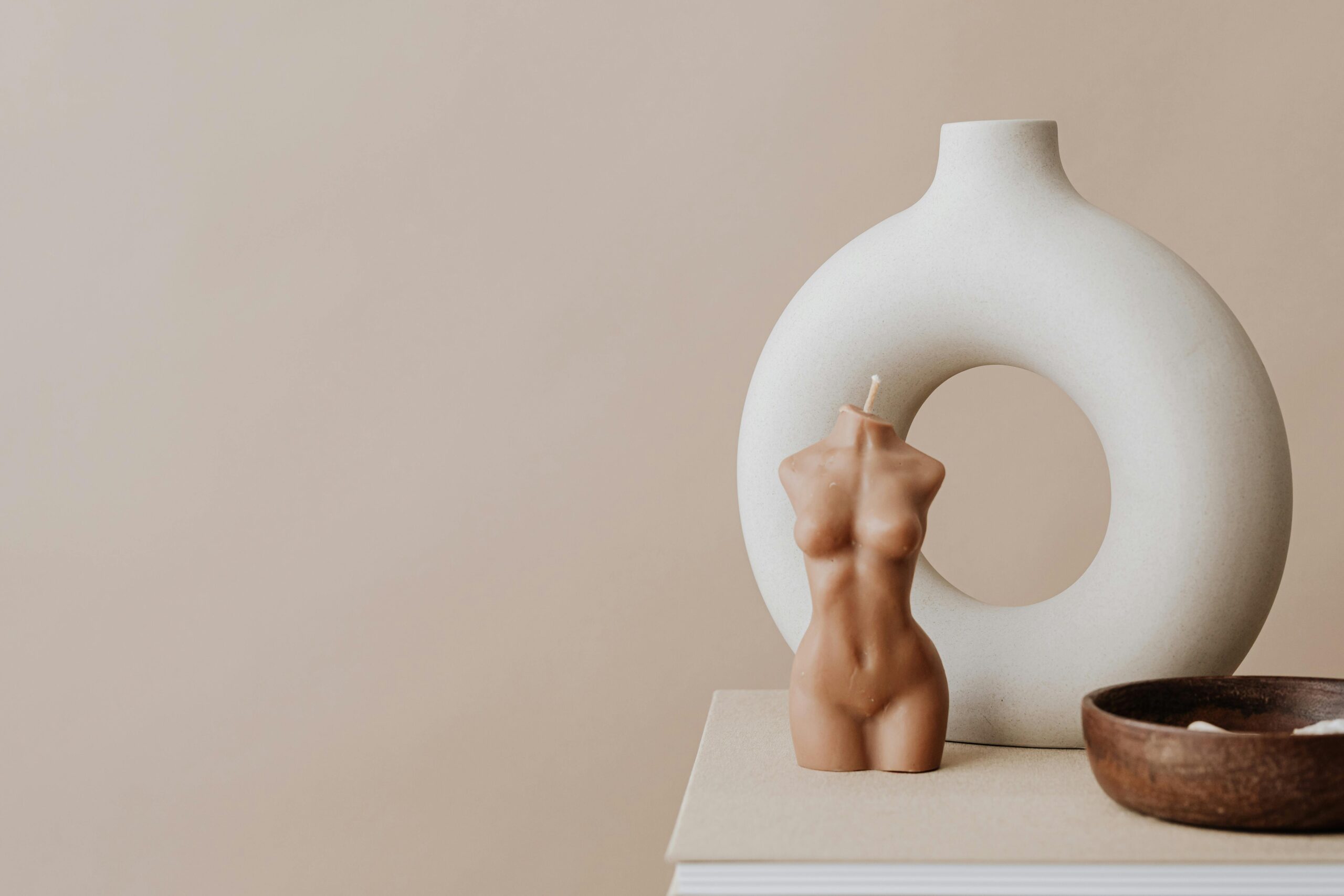 Close-up of a torso-shaped candle and sculptural vase on a beige backdrop emphasizing minimalism.